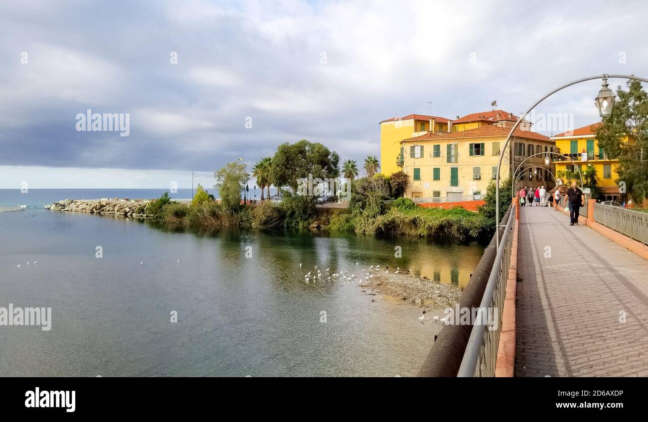 Tourists cross the bridge over the river Roia separating the two sections of Ventimiglia on the Italian Riviera. Stock Photo