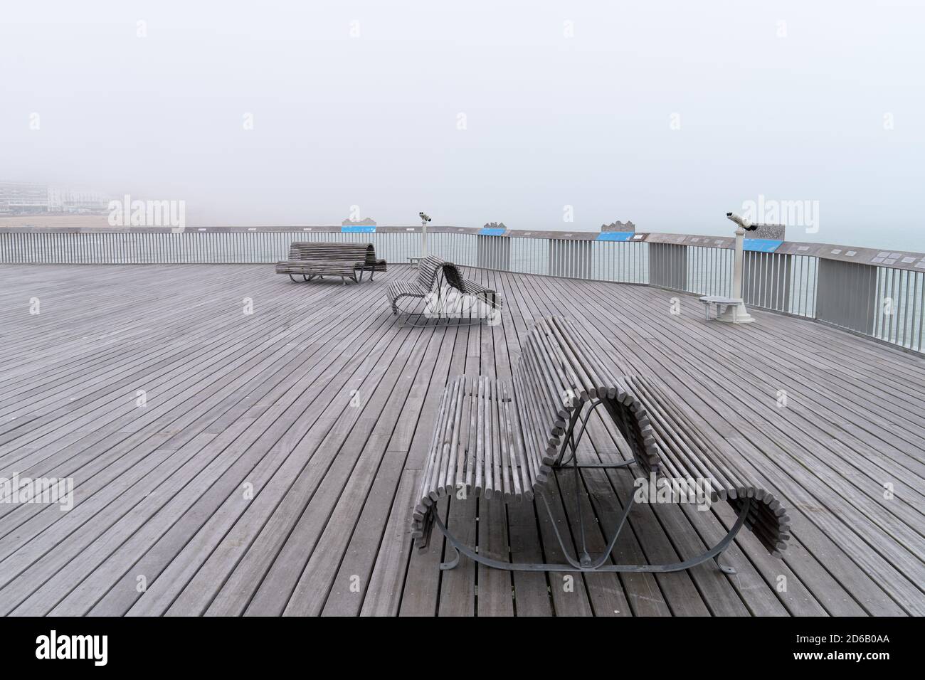 The Pier of Hastings on a misty summer day with benches and telescopes, no people, sea and buildings in the distance Stock Photo