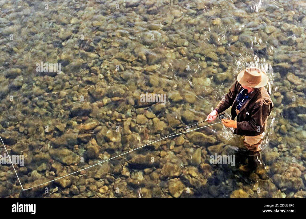 Viewed from overhead is a fly fisherman standing in the crystal-clear water of a mountain river near Sun Valley, Idaho, USA. Anglers especially enjoy casting with their fly rods into the clean freshwater streams and rivers to catch cutthroat, rainbow and other trout species that are plentiful in this scenic northwestern state. Stock Photo
