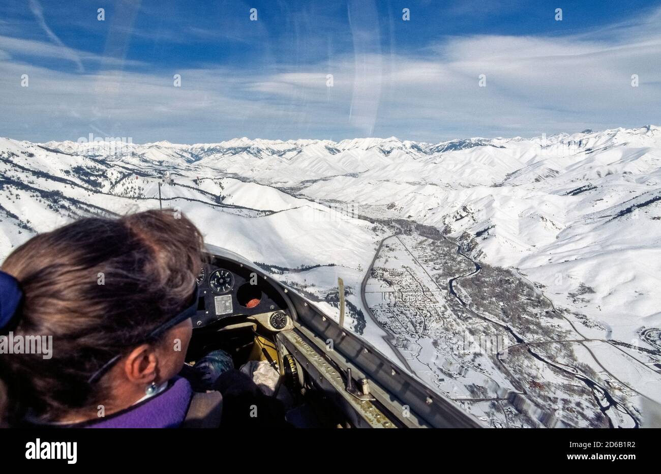A female tourist on a winter sightseeing glider flight looks through the sailplane's clear canopy at snow-covered Smoky Mountains and the Wood River Valley that's home to adjacent resort towns, Ketchum and Sun Valley, two popular vacation destinations in Idaho, USA. The scenic area boasts numerous beginner-to-expert ski trails that attract skiers and snowboarders throughout the winter season.. Stock Photo