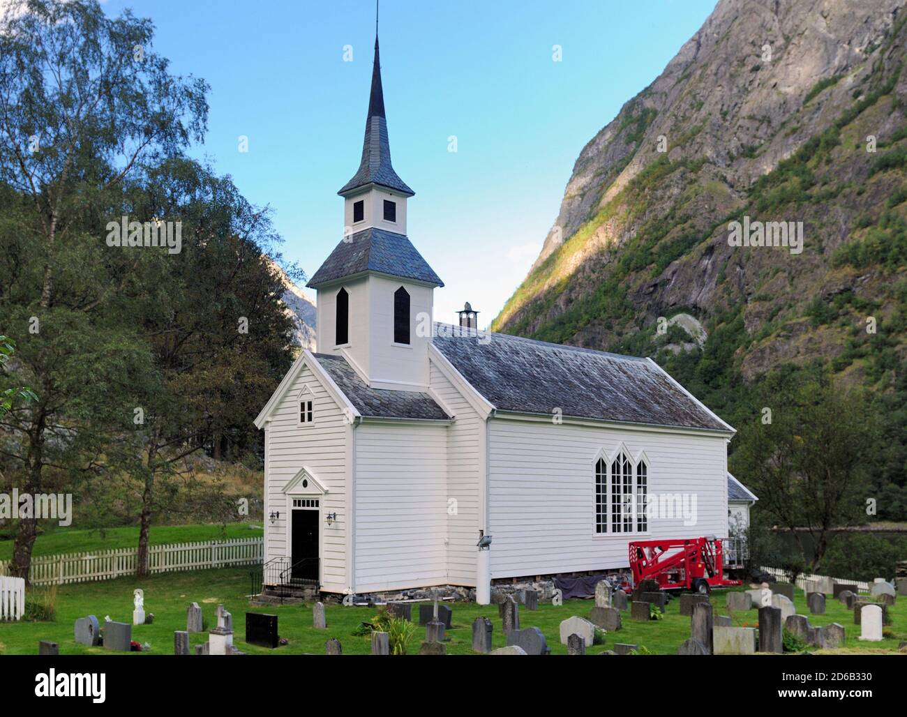 White Wooden Chapel Surrounded By Large Mountains In Undredal At Aurlandsfjord In The Late Afternoon On A Sunny Summer Day With A Clear Blue Sky And A Stock Photo