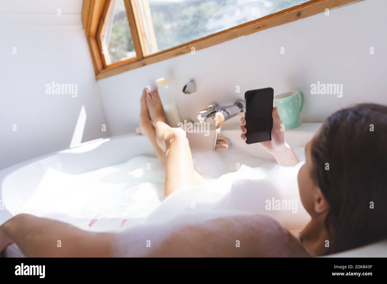 Woman using smartphone while relaxing in a bathtub Stock Photo