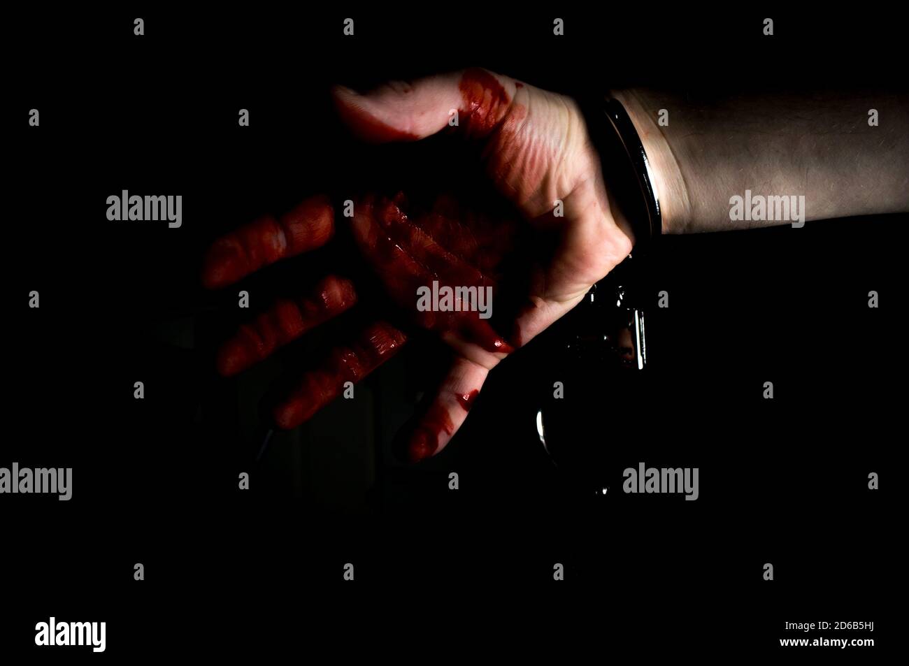 Bloody murderers hand in handcuffs in dark moody lighting Stock Photo