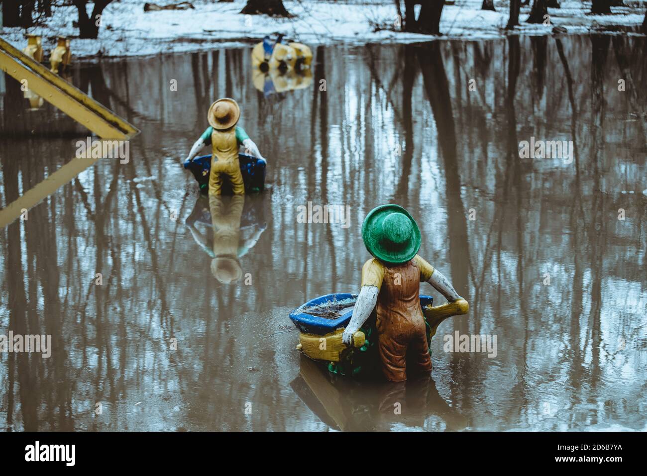 Figurines in form of gnomes stands with his back in water in spring in Russian reality. Snow is melting, creating huge puddle. Atmosphere as in fairy Stock Photo