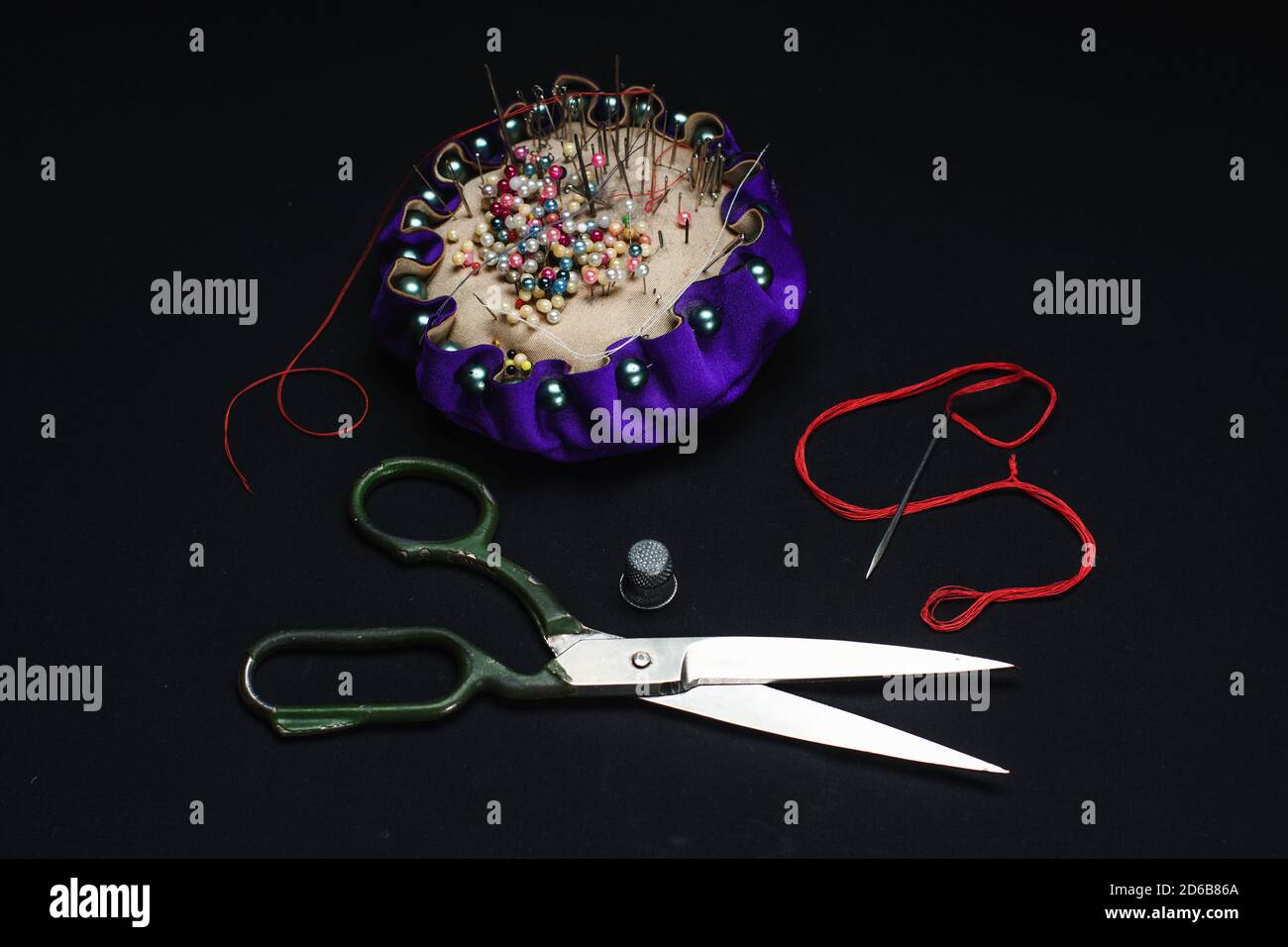 Needle bed, thimble, scissors, needle and thread on black fabric background. Stock Photo