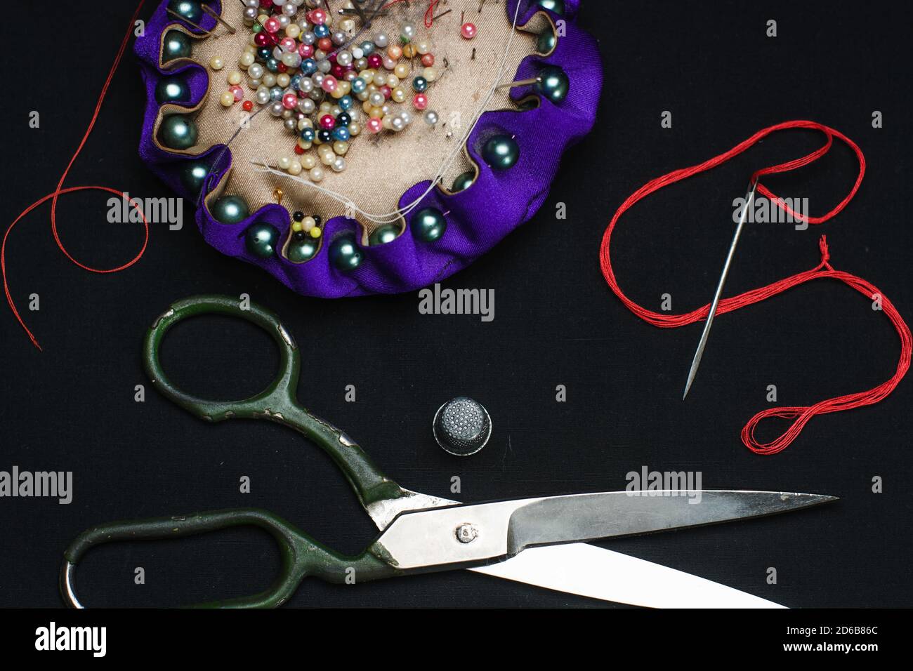 Needle bed, thimble, scissors, needle and thread on black fabric background. Stock Photo