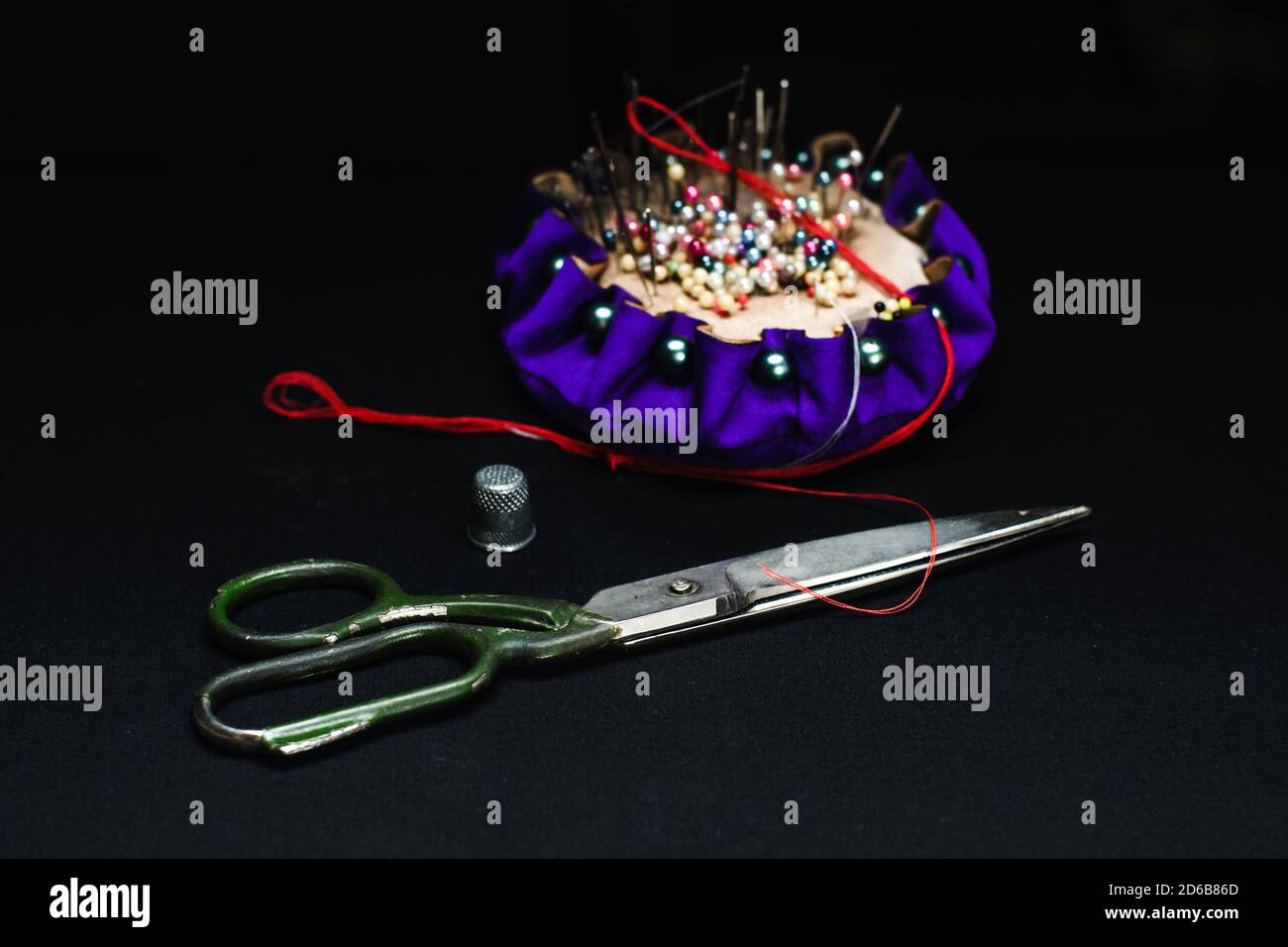 Needle bed, thimble, scissors, needle and thread on black fabric background. Stock Photo
