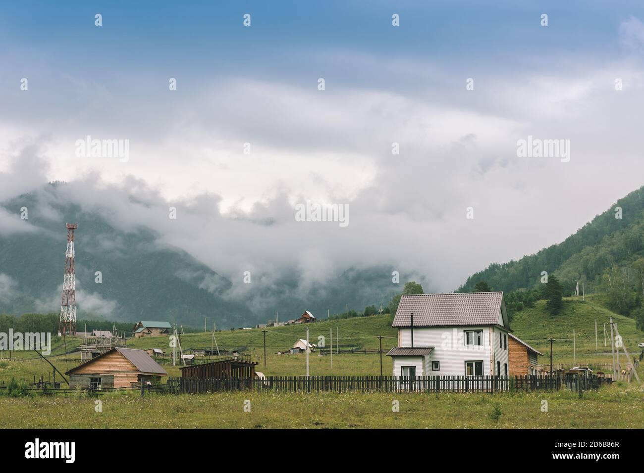 Private area with houses on background of mountains with copy space on thick fog. Vintage foggy landscape of majestic nature in faded green tones. Opa Stock Photo