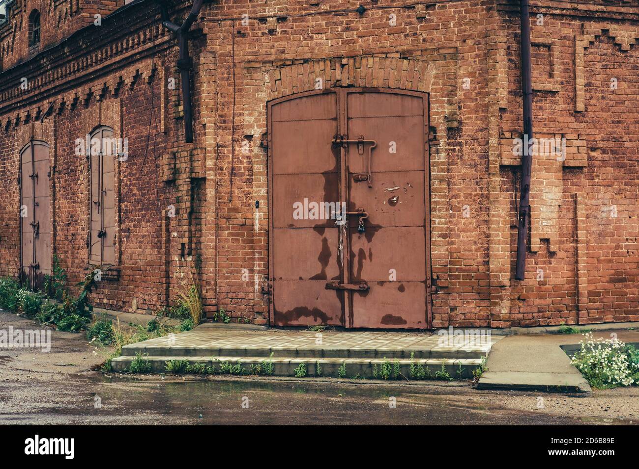 Old red brick building with huge iron locked gate in rainy weather
