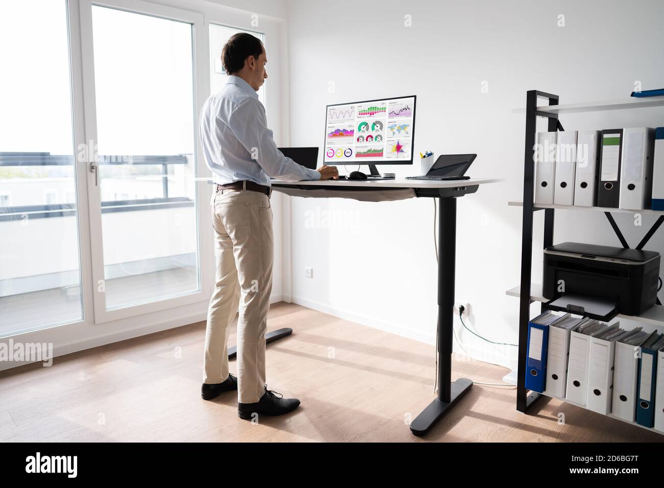 Man Working On Computer At Standing Desk In Home Office Stock Photo