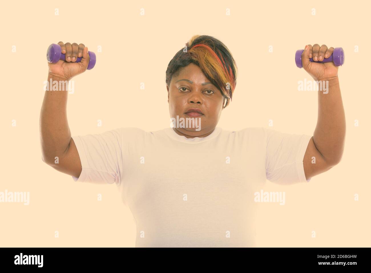 Studio shot of fat black African woman with both dumbbells raised ready ...
