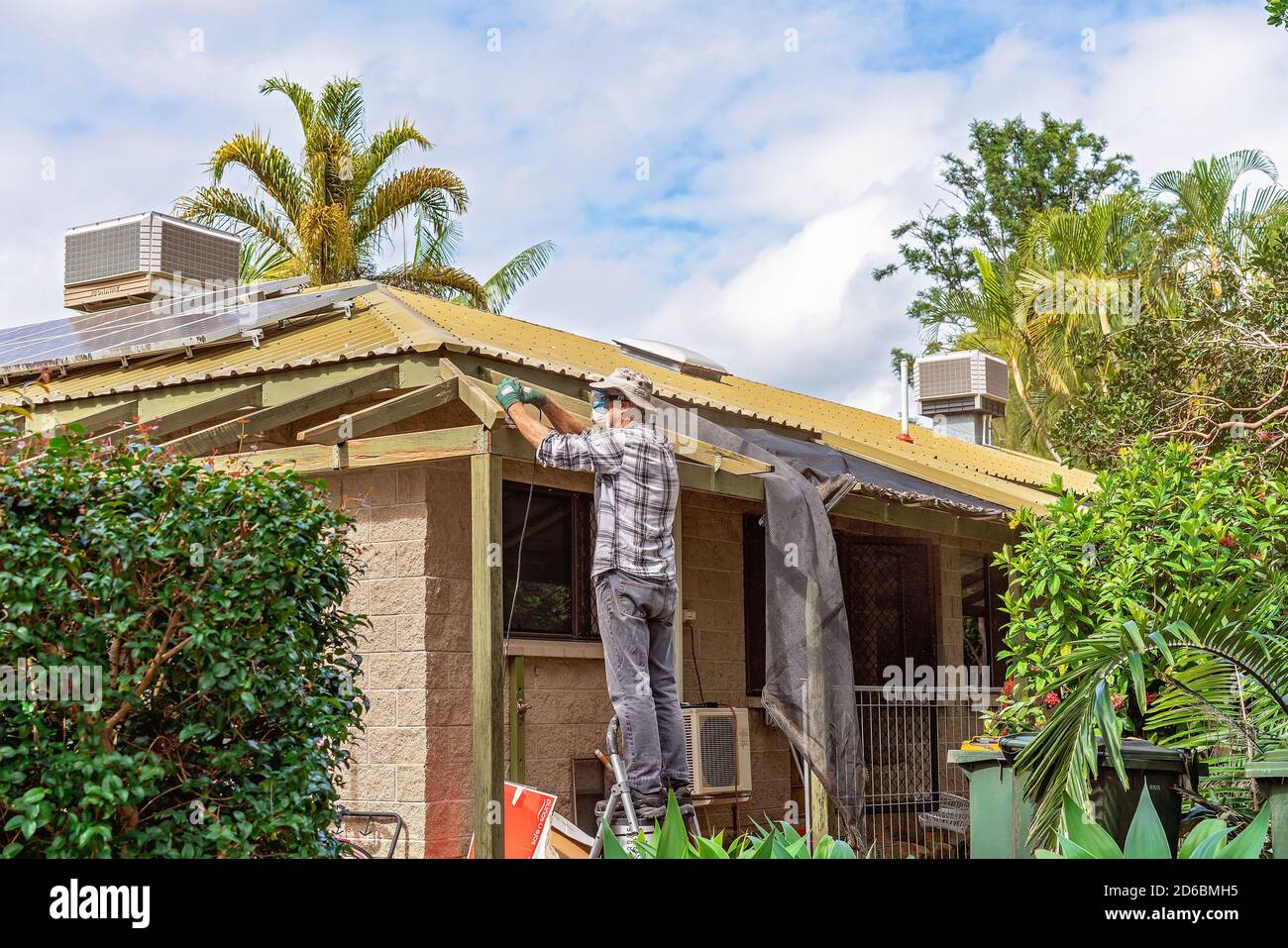 Townsville, Queensland, Australia - June 2020: Man standing on trestles sanding roof rafters of residential house Stock Photo