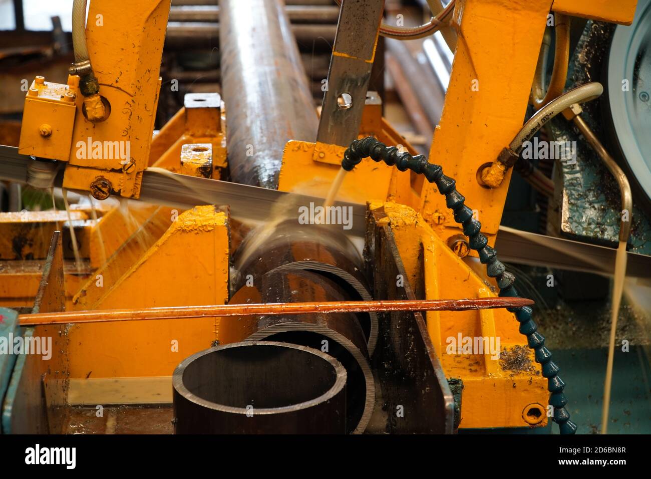 Industrial band saw, cutting metal pipe, coolant in yellow scene