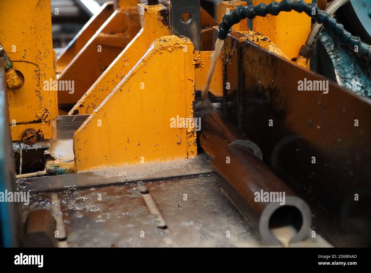 Industrial band saw, cutting metal pipe, coolant in yellow scene