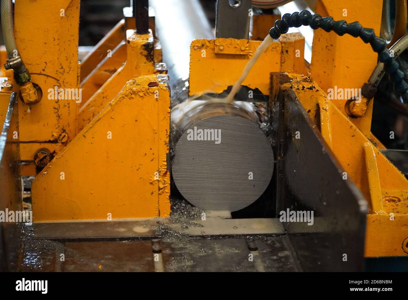 Industrial band saw, cutting metal pipe, coolant in yellow scene