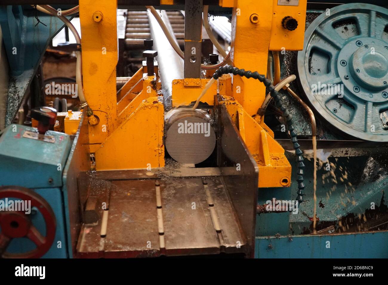 Industrial band saw, cutting metal pipe, coolant in yellow scene