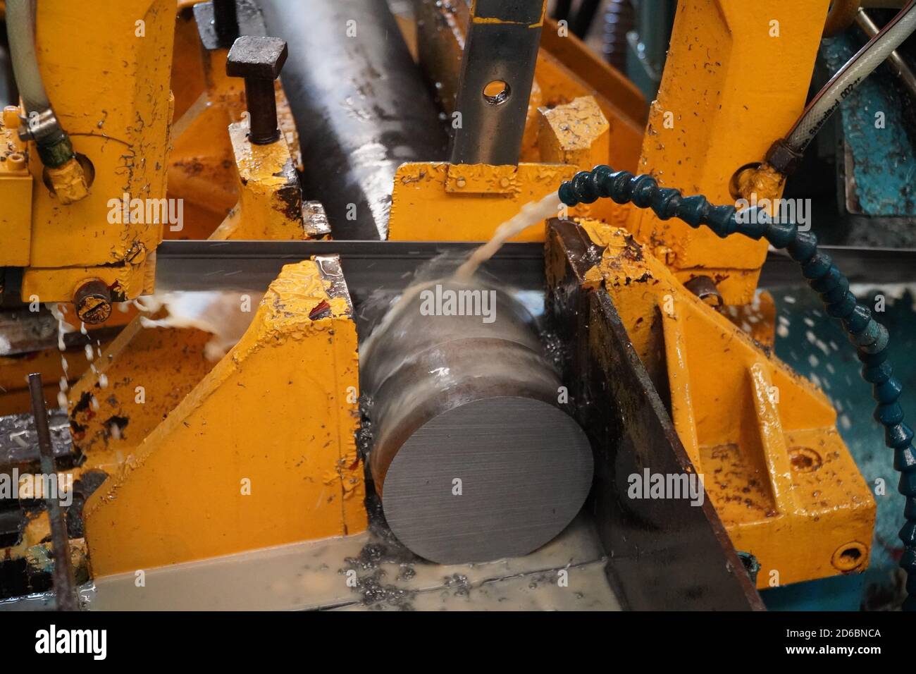 Industrial band saw, cutting metal pipe, coolant in yellow scene