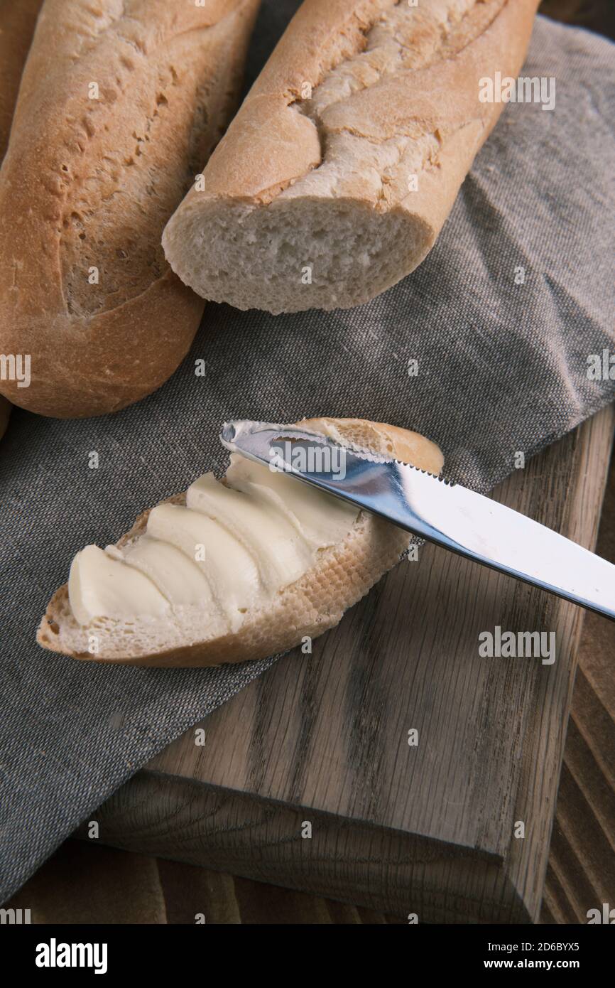 Close up fresh sliced French baguette with butter on a linen cloth with knife on a wooden table Stock Photo