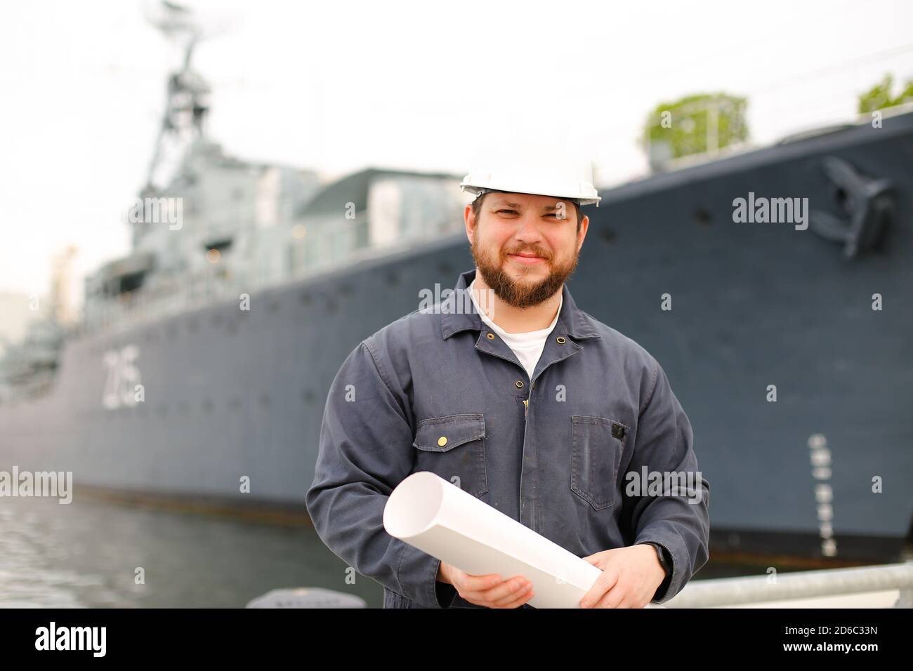 Marine chies officer holding blueprints and standing near vessel. Stock Photo