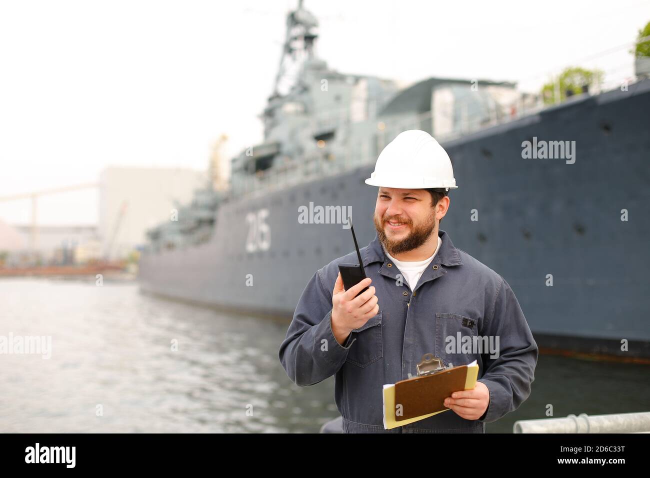 Marine first mate talking by walkie talkie and standing near vessel with documents. Stock Photo
