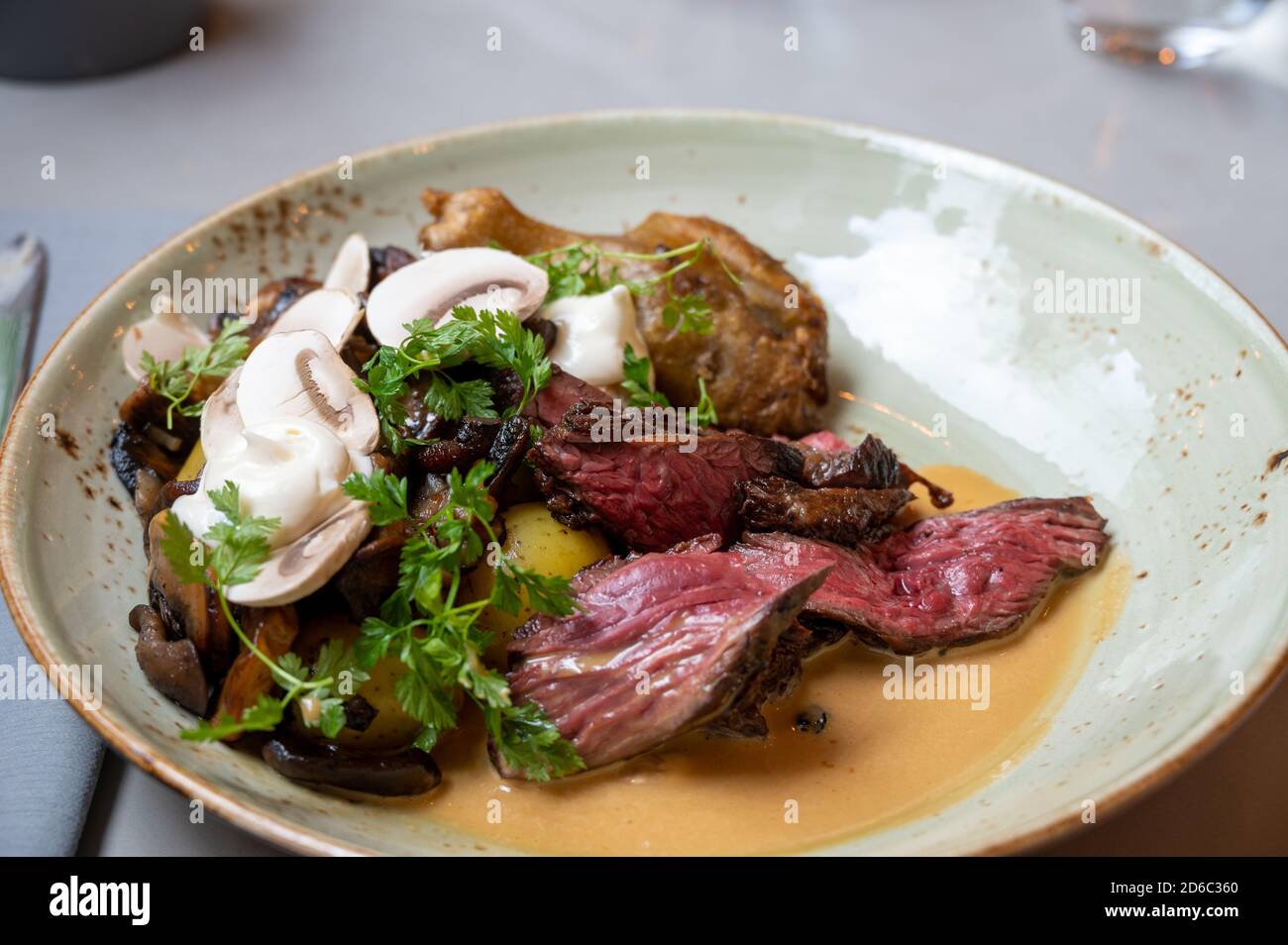 A meal based around butchers steak with mushrooms and tomatoes served in a gray rustic plate in restaurant setting Stock Photo