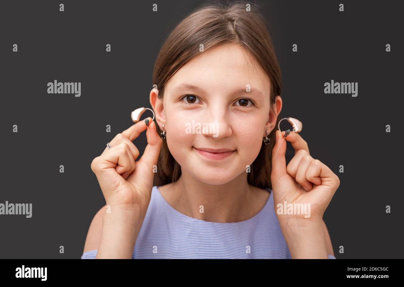 Teenage girl showing her modern hearing aids, close-up on a black background. Selection of hearing aids for a child Stock Photo