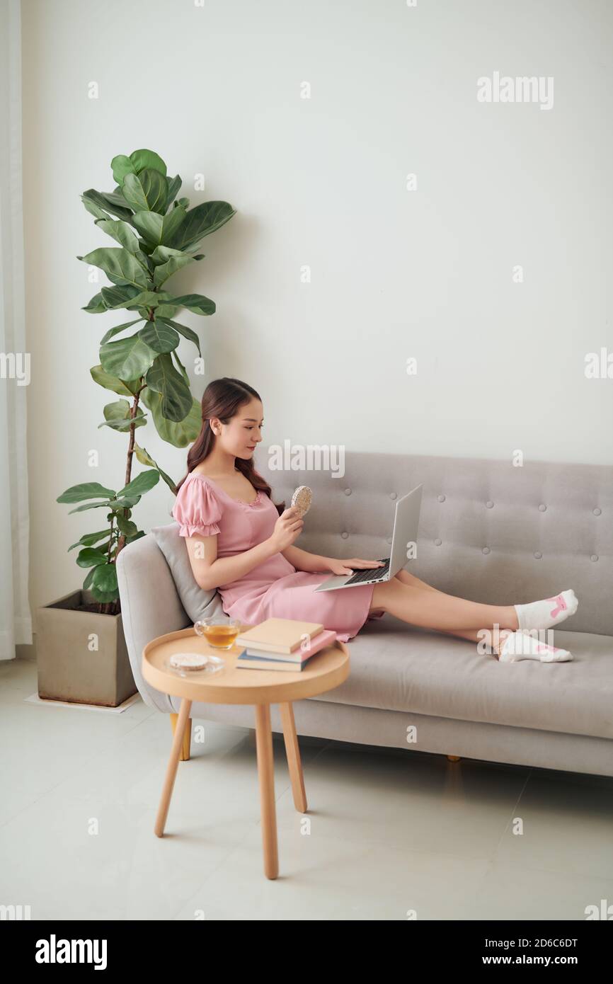 Beautiful young Asian woman using laptop while sitting at living room ...