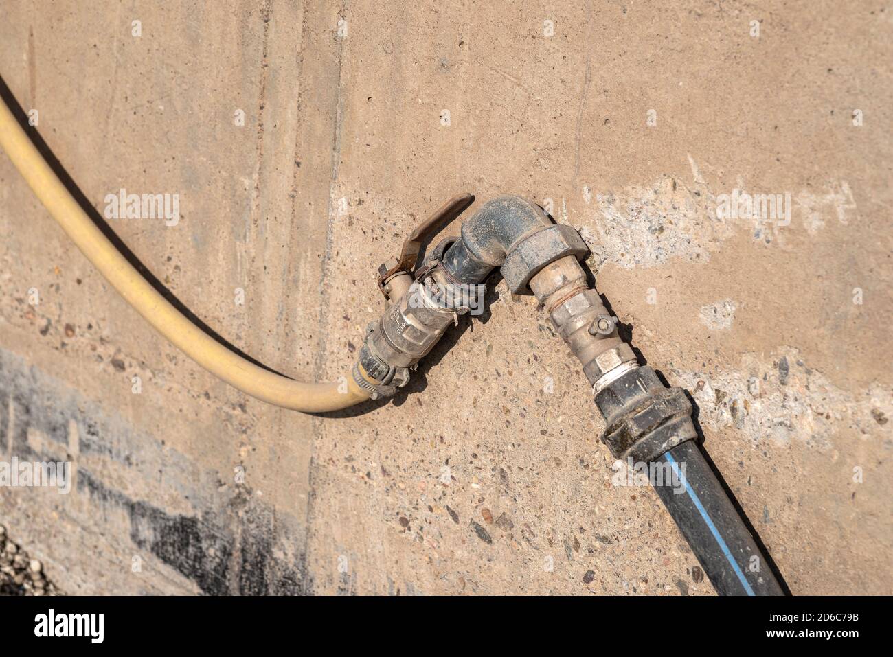 Old water valve connected to a hose, in the factory installed outside by the wall. Stock Photo