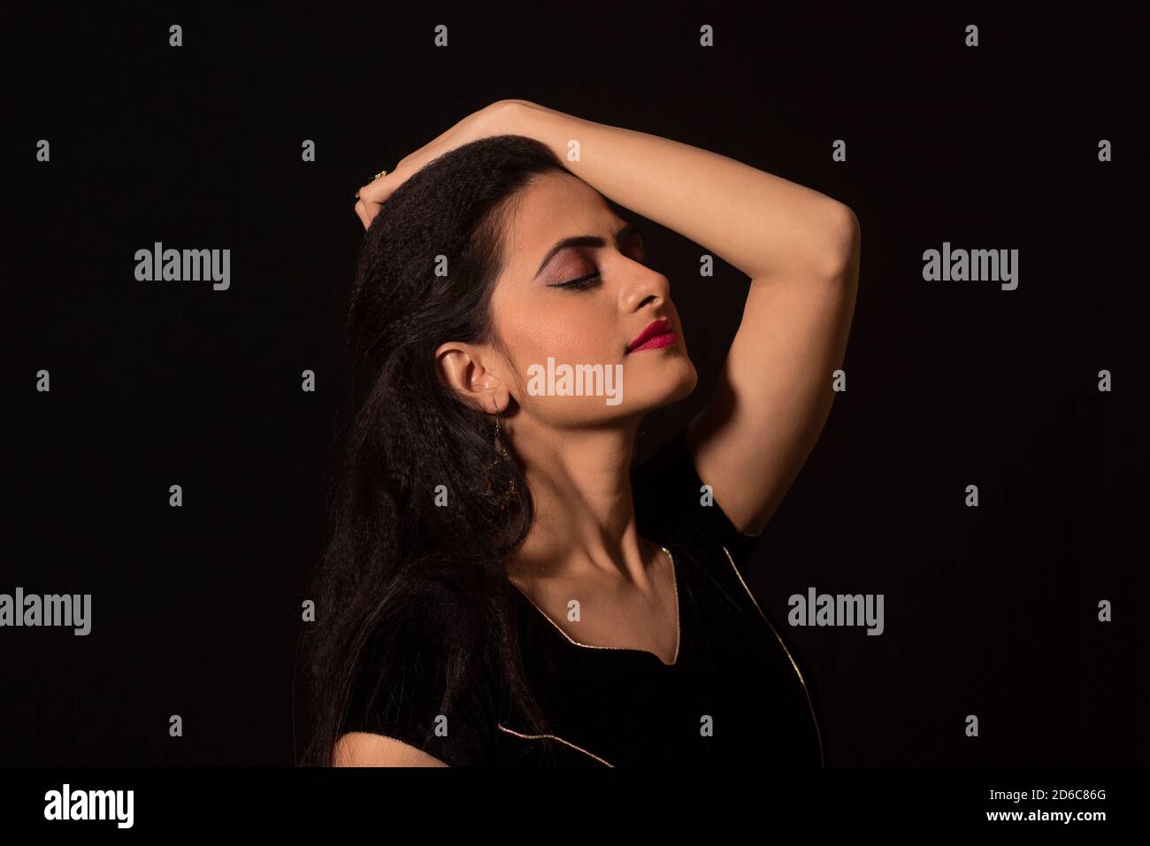 Young Indian female model with eyes closed and hand on head. Black background Stock Photo