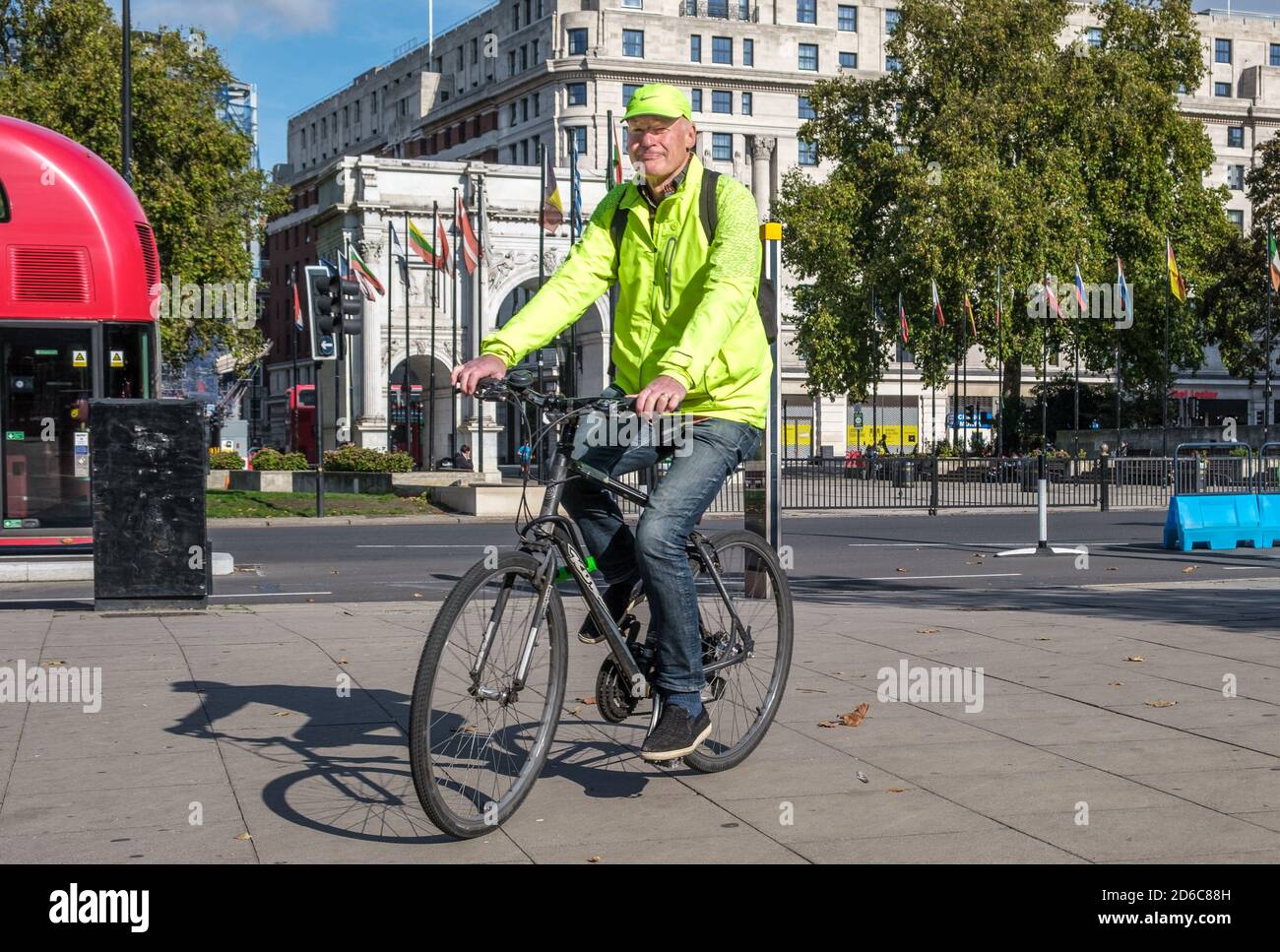 Man in yellow jacket and cap rides a bicycle in front of Marble Arch