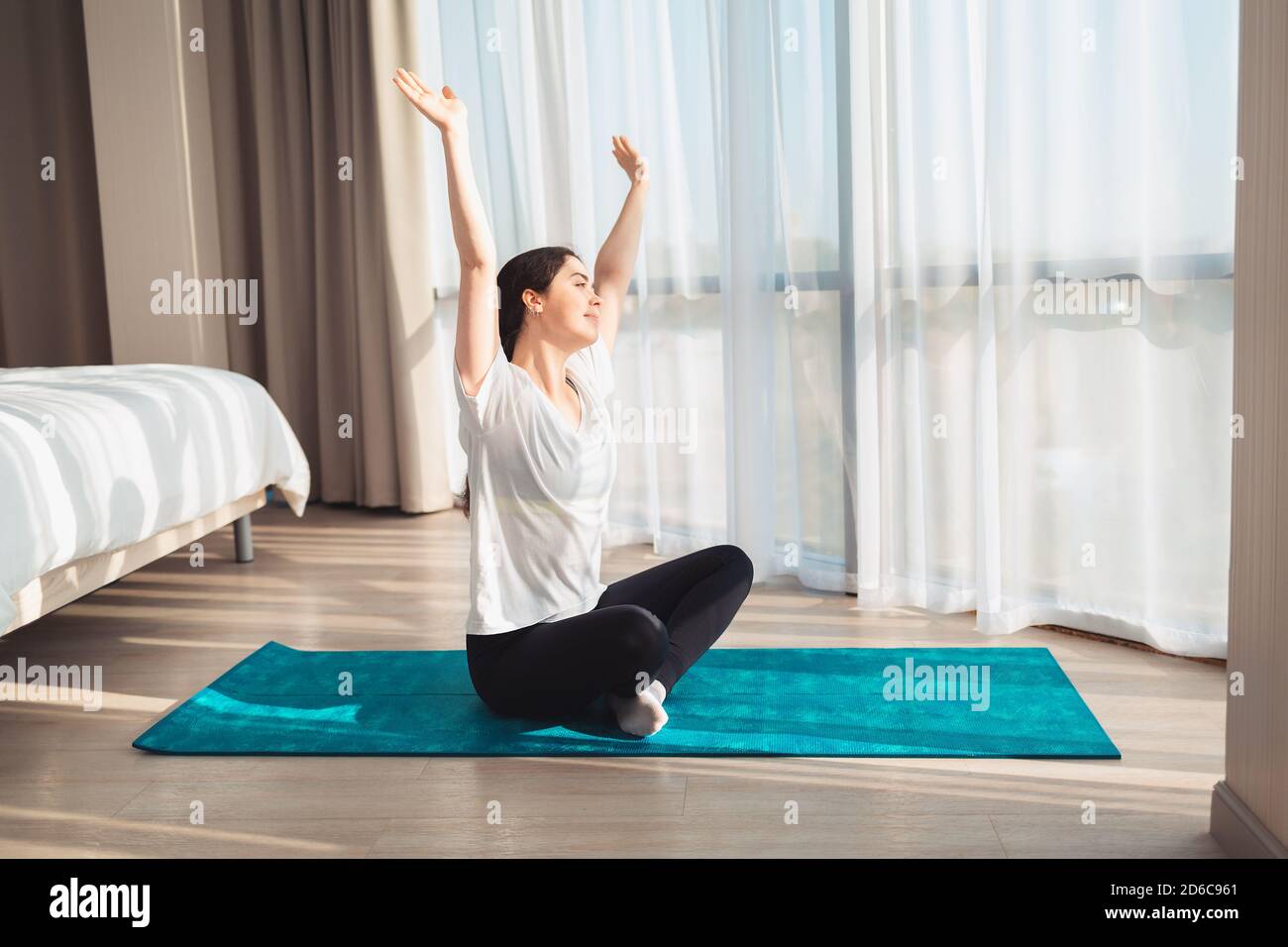 Yoga. A young beautiful woman is sitting on a sports Mat, looking out ...