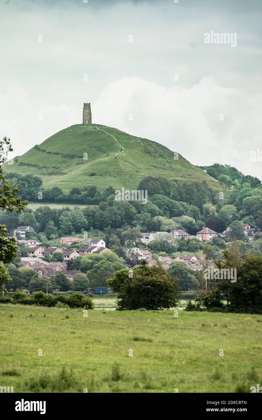 Mysterious Glastonbury Tor reigns over the New Age town of Glastonbury, England. Summer greenery and farmland in the foreground gives an idyllic vibe. Stock Photo