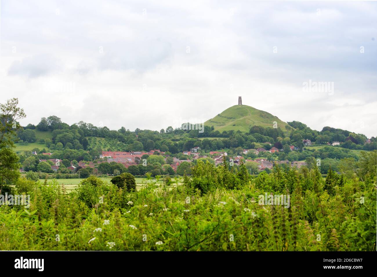 Glastonbury, England green field in foreground of red-roofed Glastonbury town. Glastonbury Tor towers in the background. Lots of copy-space. No people. Stock Photo