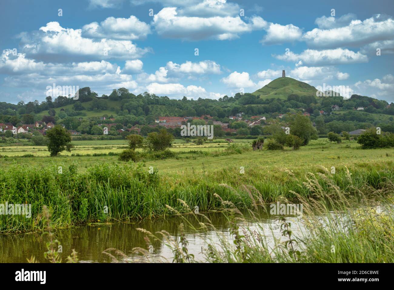 Glastonbury Tor in the distance on a bright, sunny day. Somerset, England. Tor on right of image with a local stream and farmland in foreground. Stock Photo