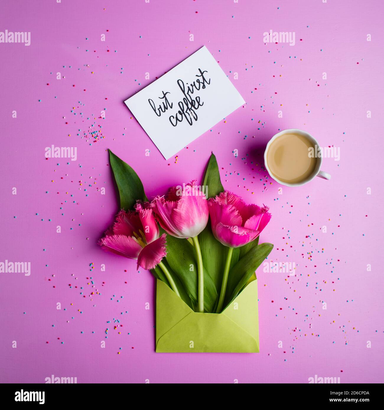 Tulips in a light green envelope, a cup of coffee with milk and a card with the inscription. Stock Photo
