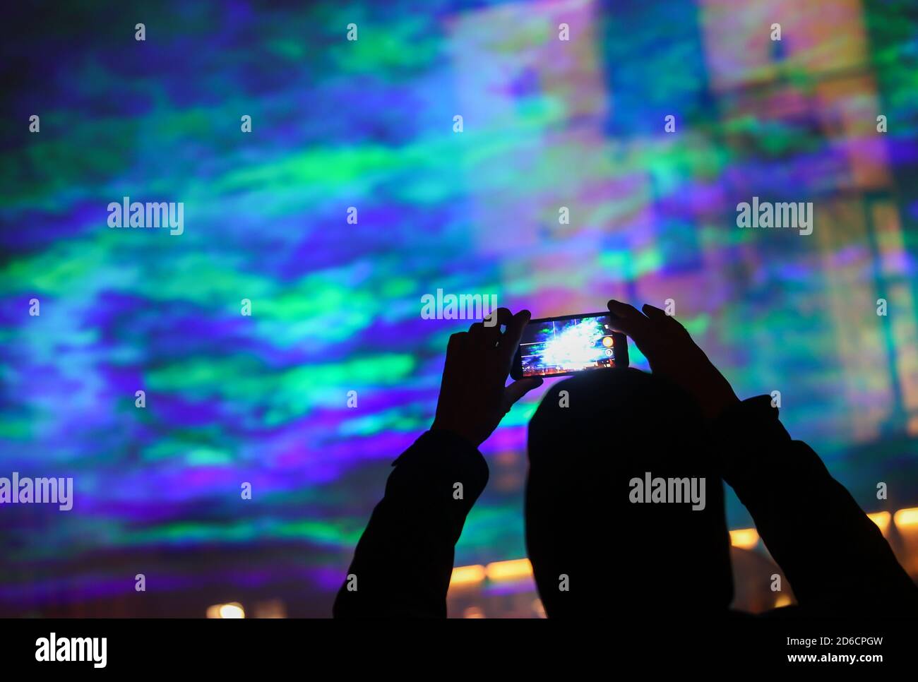 15 October 2020, Saxony-Anhalt, Halle (Saale): A passer-by takes pictures  of artificially generated auroras on the Hallmarkt using laser beams and  fog. The light installation entitled "Borealis" by Swiss artist Dan Acher