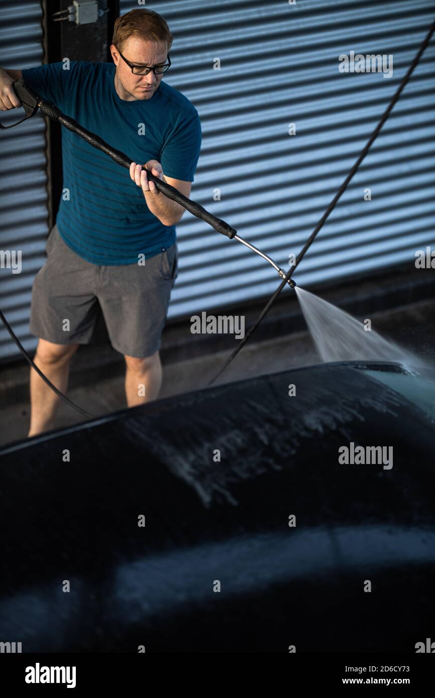 Young man washing his beloved car carefully in a manual car wash to