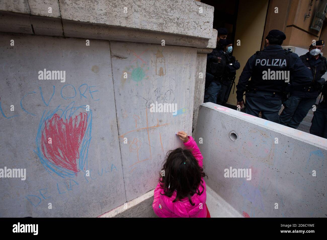 A little girl is drawing with chalks next to policemen out of Regional Government building during a protest against the closure of the schools. On October 15 the President of Campania region signed a decree ordering the closure of all schools and universities to stop the spread the second wave of covid-19 disease. Stock Photo