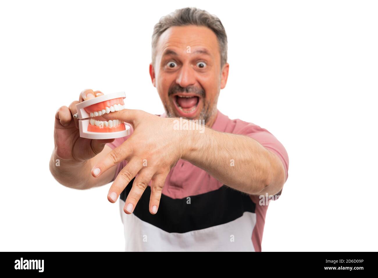 Close-up of shocked adult man having hand thumb finger bitten by fake teeth denture wearing casual summer stylish tshirt isolated on white background Stock Photo
