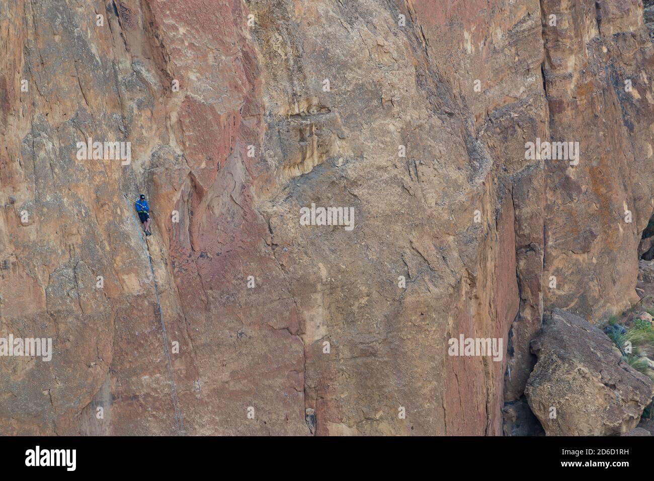 Unidentifiable solo rock climber taking a break on the smallest of ledges on the side of Smith Rock just north of Bend, Oregon Stock Photo