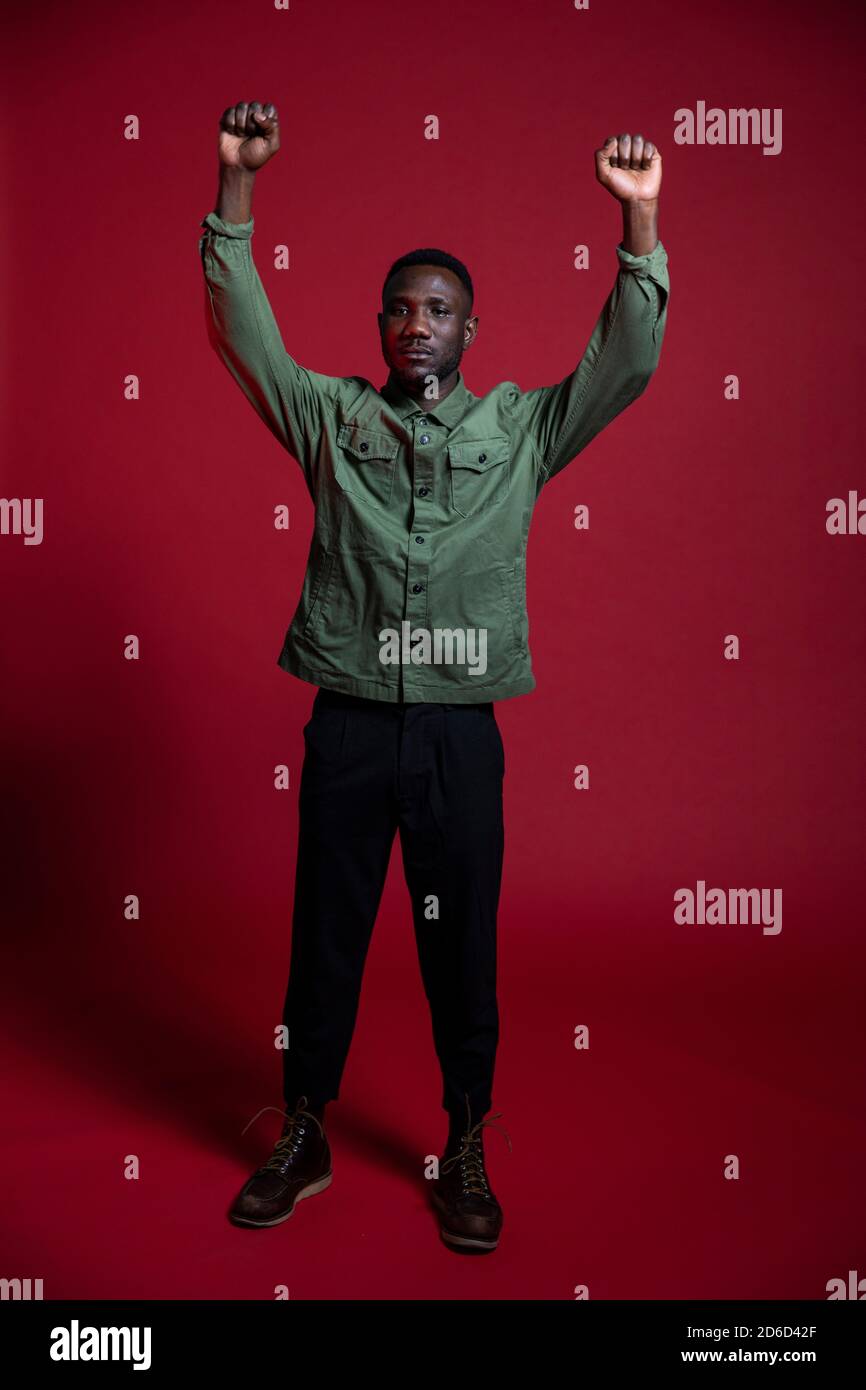 Black man raising both fists on isolated red background for professional photoshoot. Full length. Stock Photo