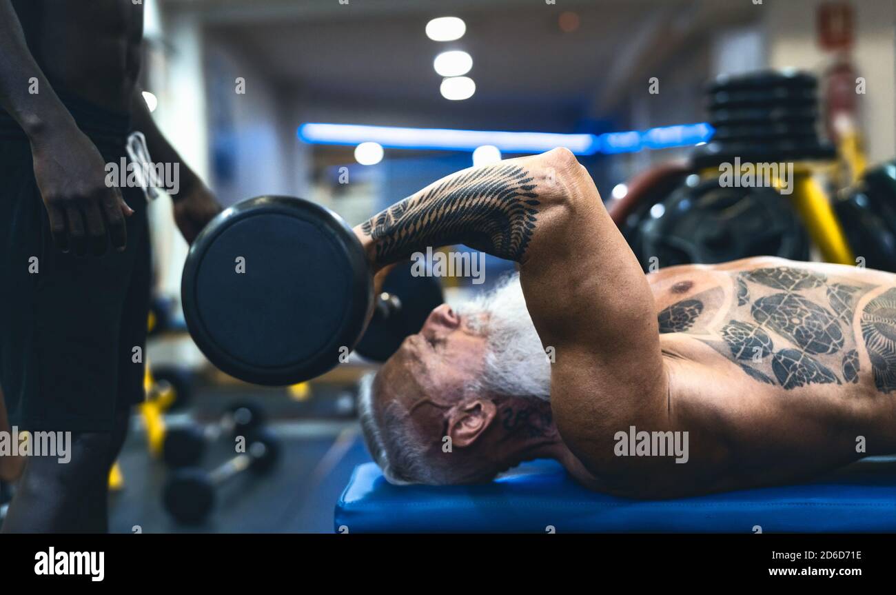 Senior fit man weight lifting with personal trainer in gym sport club