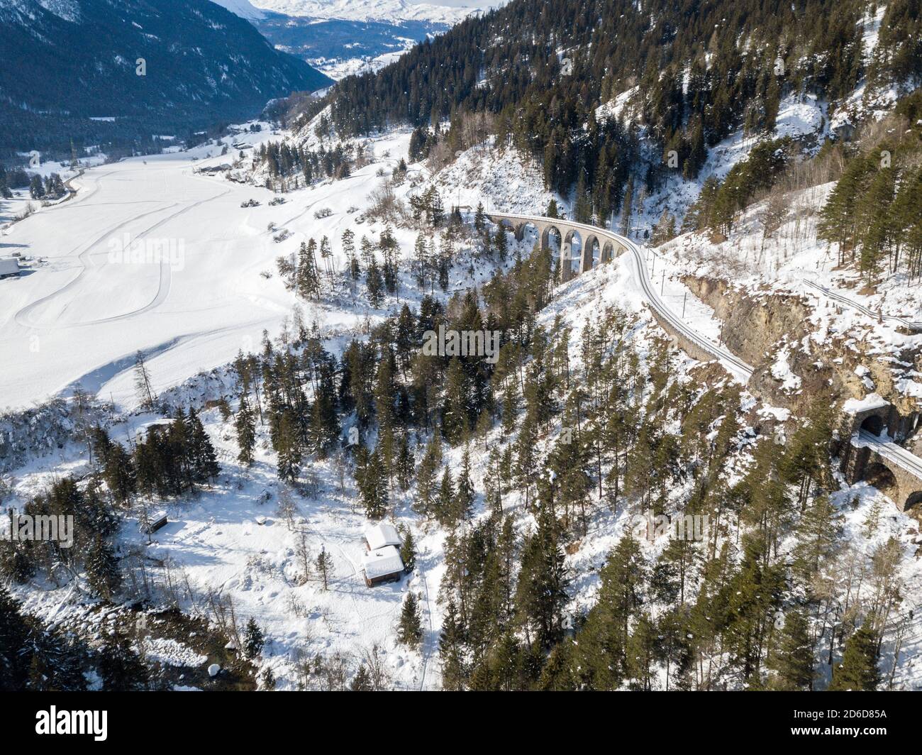 Aerial image of a mountain valley in Alps in snowy winter season with railway viaduct at the background Stock Photo