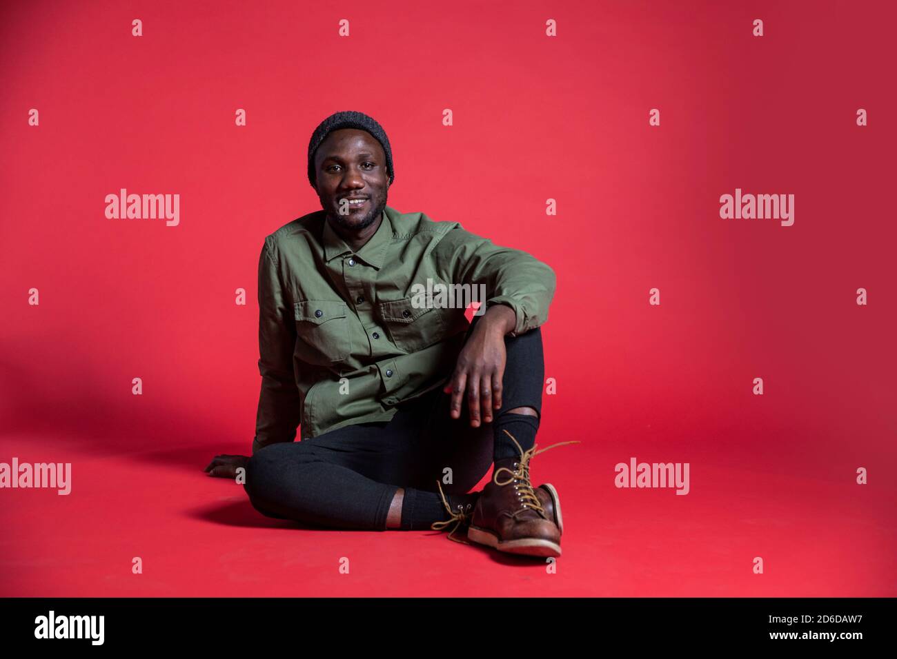 Young black man sitting relaxed on studio floor for photoshoot. Isolated. Copy space. Stock Photo