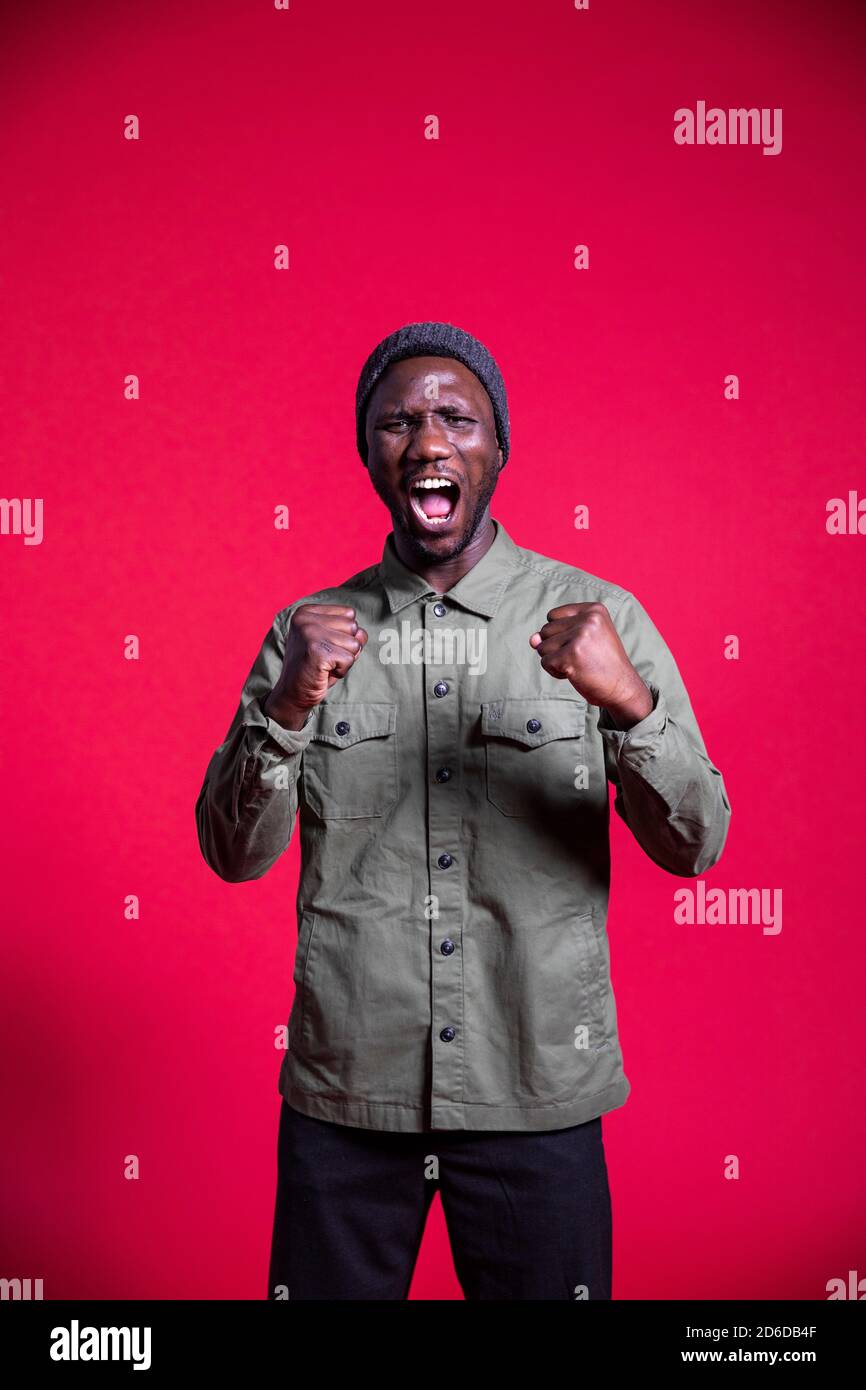 Young black man shouting with fists clenched and mouth open. Isolated. Medium shot. Stock Photo