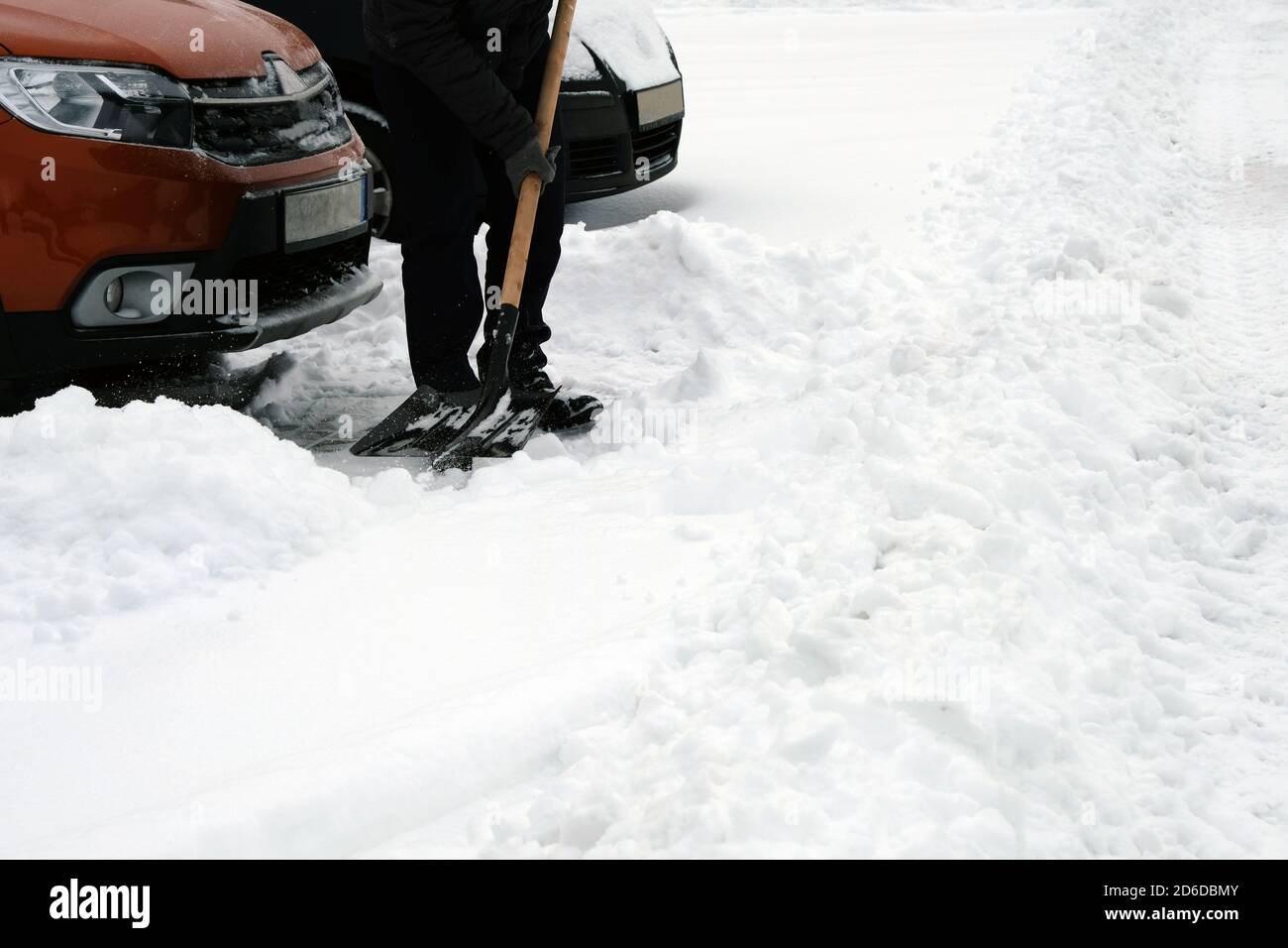 Shovel in hand. Man with shovel clears snow around car in parking lot in winter after snowfall. Winter problems of car drivers. Stock Photo