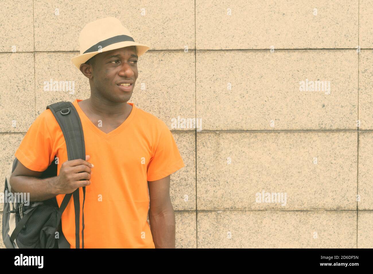 Young black African tourist man holding backpack while thinking and looking at distance against concrete block wall Stock Photo
