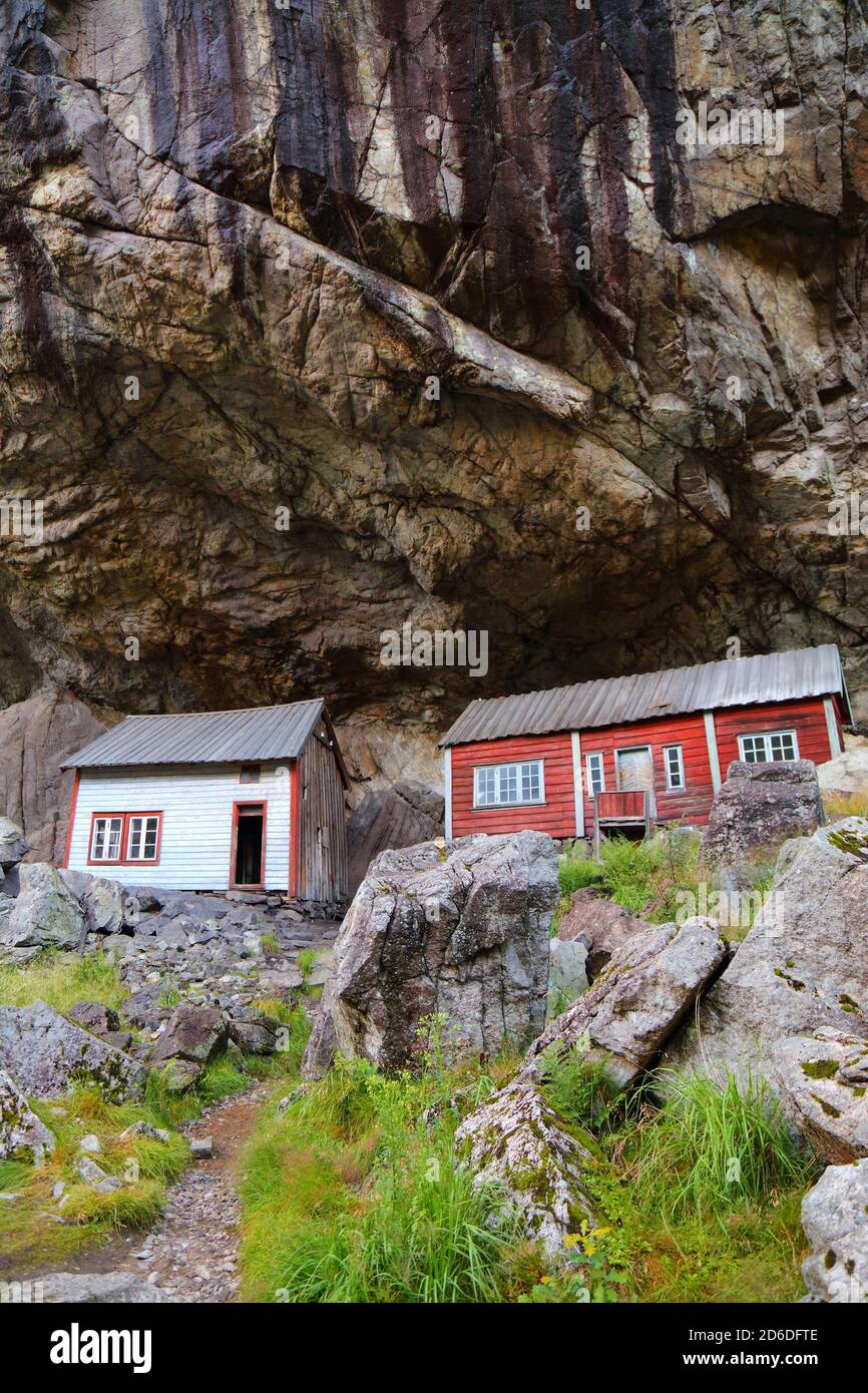 Norway landmark. Helleren old homes hidden beneath huge rock cliff in Jossingfjord. Stock Photo