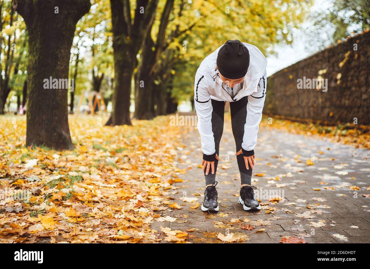 Mid aged fit athletic woman dressed modern running clothes standing and  bend over to stretch the back on the footway after jogging in the autumnal  cit Stock Photo - Alamy