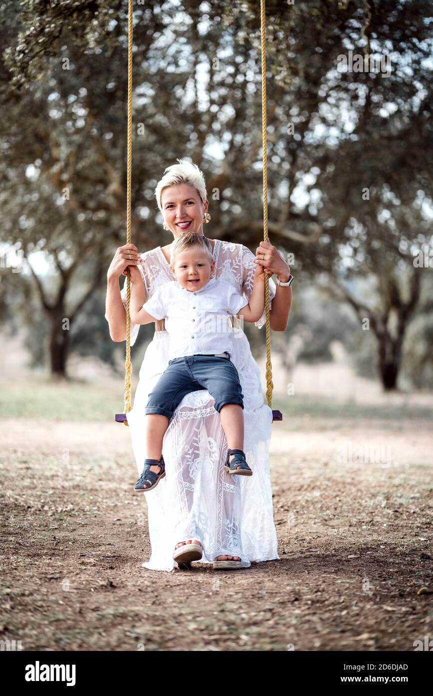 Pregnant woman having fun with her toddler son on the swing in the park Stock Photo